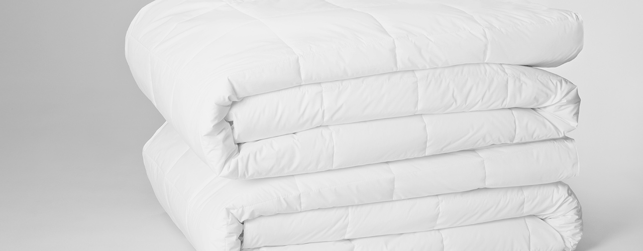 Two white, quilted blankets are stacked on a grey background.