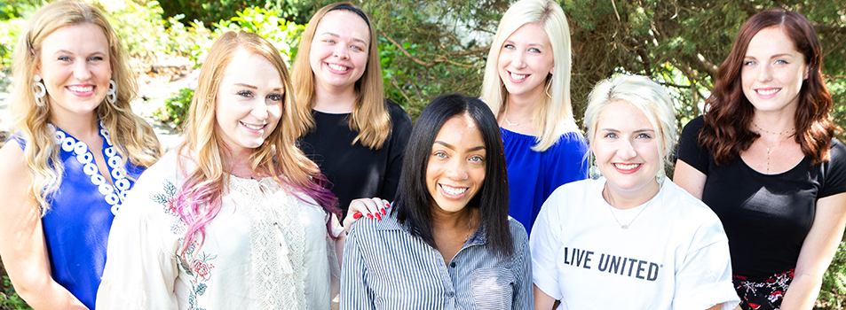 A group of women, smiling in front of a forested background.