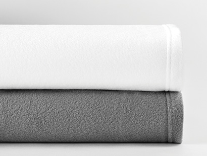 A white fleece blanket is stacked on top of a dark grey fleece blanket on a grey background.