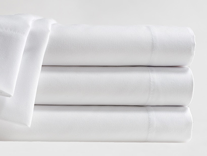 A stack of three folded white microfiber sheets, parts of a fourth sheet are draped over the stack.