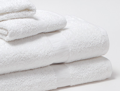 A stack of two Cam Towels with a wash cloth and hand towel placed on top, sits on a greyish-white background.